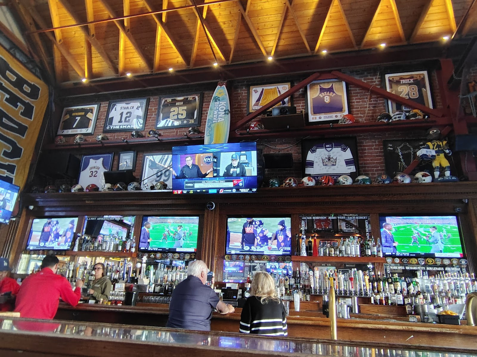 The real sports memorabilia wall at Legends Sports Bar, with autographed jerseys, helmets, and TVs above the bar